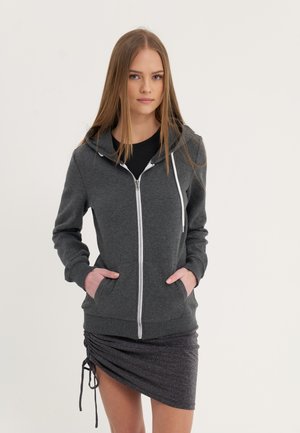 Siva zip-up hoodie izrađena od mekog materijala sa belim zipom i špagom, uparen s crnim rebrastim topom i teksturiranom naboranom suknjom.