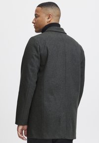Abrigo de lana gris oscuro con un corte ajustado, cuello con muesca y ventilación trasera. La tela texturizada y las líneas limpias crean un aspecto contemporáneo.
