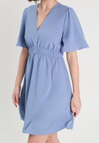 Lyseblå kjole lavet af blødt stof, med v-udskæring, korte puffærmer og elastisk talje for en afslappet pasform.