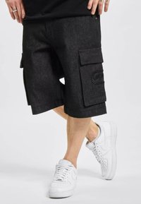 Zwarte denim cargo shorts met twee grote zijzakken en geborduurd logodetail; gecombineerd met witte sneakers.