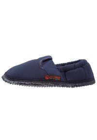 Marineblauwe stoffen pantoffel met elastische band, zachte binnenvoering en textuur rubberen zool. Voorzien van een rode label met de merknaam.