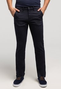 Granatowe spodnie dżinsowe o prostym kroju, z przednimi kieszeniami, zapięciem na guziki i subtelną fakturą. Połączone z niebieskimi sneakersami.