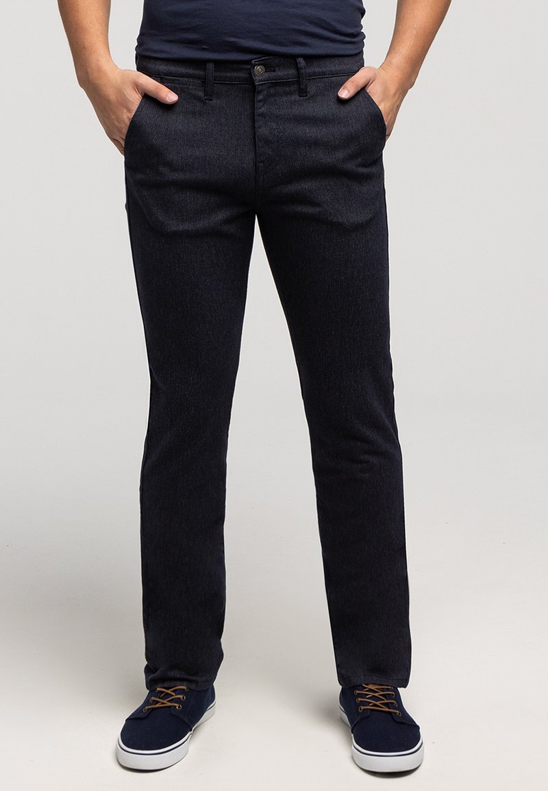 Granatowe spodnie dżinsowe o prostym kroju, z przednimi kieszeniami, zapięciem na guziki i subtelną fakturą. Połączone z niebieskimi sneakersami.