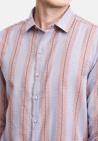 Camisa de botones con rayas verticales en azul claro y rosa, tejido texturizado, cuello con puntas y cinco botones a lo largo de la tapeta frontal.