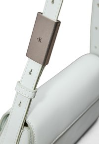 Bolso de mano de cuero blanco con una textura suave, que presenta un cierre metálico y una correa ajustable, mostrando costuras sutiles y una marca.
