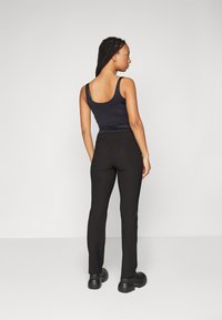 Haut sans manches noir associé à un pantalon ajusté noir. La tenue présente une texture lisse et un design simple et épuré.