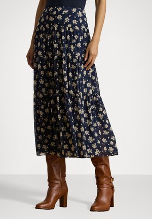 Gonna maxi floreale blu navy con design a strati; presenta piccoli fiori beige su un tessuto fluente, abbinata a stivali alti fino al ginocchio marroni con tacco.