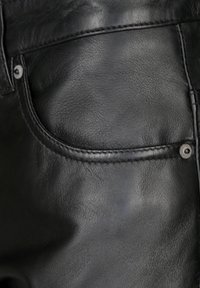 Zwarte leren jeans met een gladde textuur, contrasterende stiksels en een zichtbare zak. Inclusief een metalen drukknoopdetail.