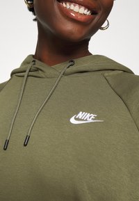 Oliwkowa bluza z kapturem Nike z białym logo na lewej piersi; wyposażona w kaptur z troczkiem i teksturowaną tkaninę.