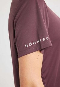 Maglietta atletica a maniche corte di colore bordeaux, realizzata in un tessuto liscio, con un logo "RÖHNISCH" bianco sulla manica sinistra e cuciture ben curate.