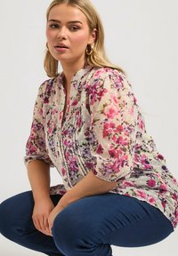 Kukkakuosiset puserot, joissa on violetteja, vaaleanpunaisia ja valkoisia kuvioita; läpikuultava kangas, napitettu etuosa ja 3/4-puffihihat. Yhdistettyinä tummansinisiin farkkuihin.