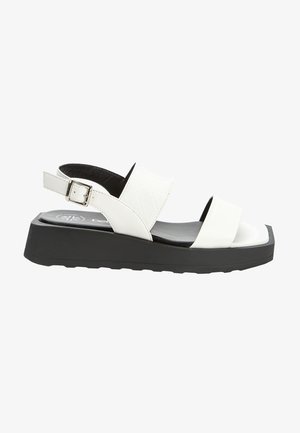 Sandale blanche à bout ouvert avec deux larges brides, une semelle noire matelassée et une boucle de cheville ajustable sur un talon plateforme épais.