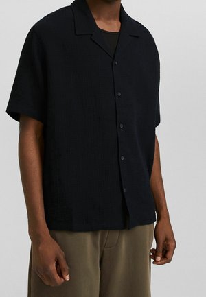 Zwarte button-up shirt met korte mouwen van een textuurstof, een platte kraag en een relaxte pasvorm, gecombineerd met lichtbruine broek.