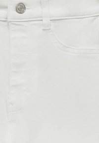 Jean en denim blanc en gros plan montrant le bouton, la boucle de ceinture et les détails de couture de la poche avant.