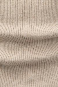 Bēšs ribots audums ar mīkstu tekstūru, kas izceļ īsas vertikālas svītras un smalkas toņu nianses, veidojot maigumu un siltumu.