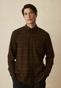 Camicia a quadri marrone con tonalità verde scuro, rosso e beige, chiusura con bottoni sul davanti, colletto e maniche lunghe, realizzata in tessuto morbido.