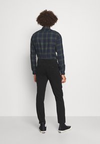 Grön och marinblå rutigt skjorta, långa ärmar, knapp-down krage, i kombination med svarta avsmalnande byxor och svarta högskostrumpor.