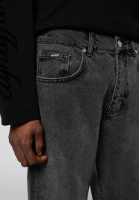 Black denim jeans with a fitted design, featuring a classic five-pocket style, visible stitching, and a textured fabric.