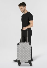 Maleta rígida gris con un diseño estampado, protectores de esquina negros, asa telescópica y ruedas suaves.