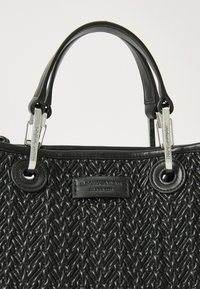 Fekete szőtt táska texturált felülettel, dupla fekete fogantyúval, ezüst hardware részletekkel és logóval debütált bőr címkével.