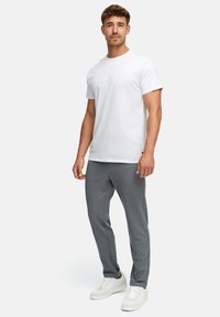 Weißes Baumwoll-T-Shirt, kombiniert mit grauen Jogginghosen. Das Modell trägt weiße Sneakers. Einfaches Design, kurze Ärmel und lockere Passform.