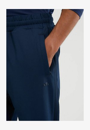 Granatowe spodnie sportowe wykonane z gładkiego materiału, z elastycznym paskiem w talii, bocznymi kieszeniami oraz małym logo marki na udzie.