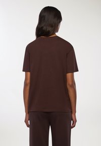 Brązowa bawełniana koszulka z okrągłym dekoltem, krótkim rękawem i luźnym krojem, pokazana od tyłu. Brak widocznych wzorów lub grafik.