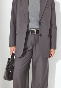 Pilkai pritaikyta švarkas su atitinkamomis plačiomis kelnėmis. Po juo uždėtas tekstūruotas pilkas megztinis; juodas diržas ir blizgi juoda rankinė.