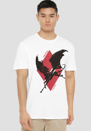 Young man wearing a white t-shirt with a black winged horse graphic over a red diamond shape and the word "THESTRAL" on front.