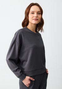 Felpa grigia con maniche lunghe, scollo rotondo e fit rilassato. Realizzata in materiale morbido con una texture liscia. Include un orlo a coste.