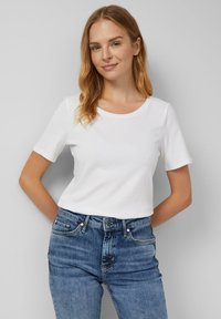Weißes Baumwoll-T-Shirt mit kurzen Ärmeln und Rundhalsausschnitt, kombiniert mit blauen Jeans; glatte Textur und klassischer Schnitt.