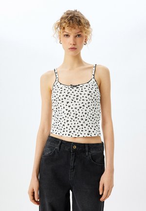 Top corto blanco con patrón floral negro, tirantes finos y un borde festoneado. Combinado con unos vaqueros de denim negro de cintura alta.