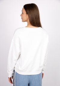 White sweatshirt with a relaxed fit, ribbed cuffs, and hem, featuring a wide neckline. Paired with light blue denim pants.
