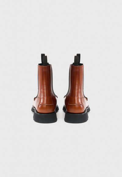 Brązowe skórzane botki za kostkę z elastycznymi panelami po bokach, pętelkami do ściągania i czarną, teksturowaną gumową podeszwą. Gładkie wykończenie o minimalistycznym designie.