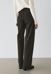 Donkerbruine high-waisted jeans met een rechte pijp, voorzien van twee achterzakken en een gladde textuur. Gecombineerd met een lichtgekleurd topje.