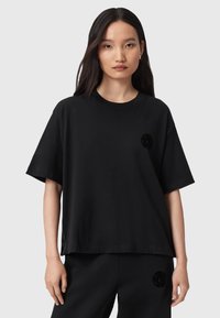 T-shirt oversize in cotone nero con maniche corte, scollatura tonda e un logo testurizzato sottile sul lato sinistro del petto. Tessuto morbido.