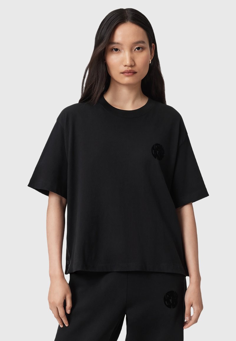 T-shirt oversize in cotone nero con maniche corte, scollatura tonda e un logo testurizzato sottile sul lato sinistro del petto. Tessuto morbido.