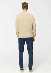 Pulover bej cu guler, manșete și tiv țesute. Purtați cu pantaloni negri adaptați și adidași de culoare deschisă.