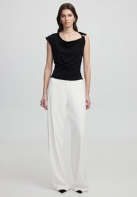 Černý top s širokými rukávy, zdobený stříbrným akcentem na jednom rameni. V kombinaci s volnými bílými kalhotami a černými špičkami.