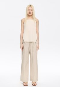 Light beige ribbed sleeveless top with side slits, paired with loose-fitting beige pants featuring drawstrings and two front pockets.
