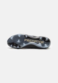 Voetbalschoen met een zwarte zool, een gestructureerd oppervlak en opvallende noppen. Met "PREDATOR" in gouden letters langs de zijkant.