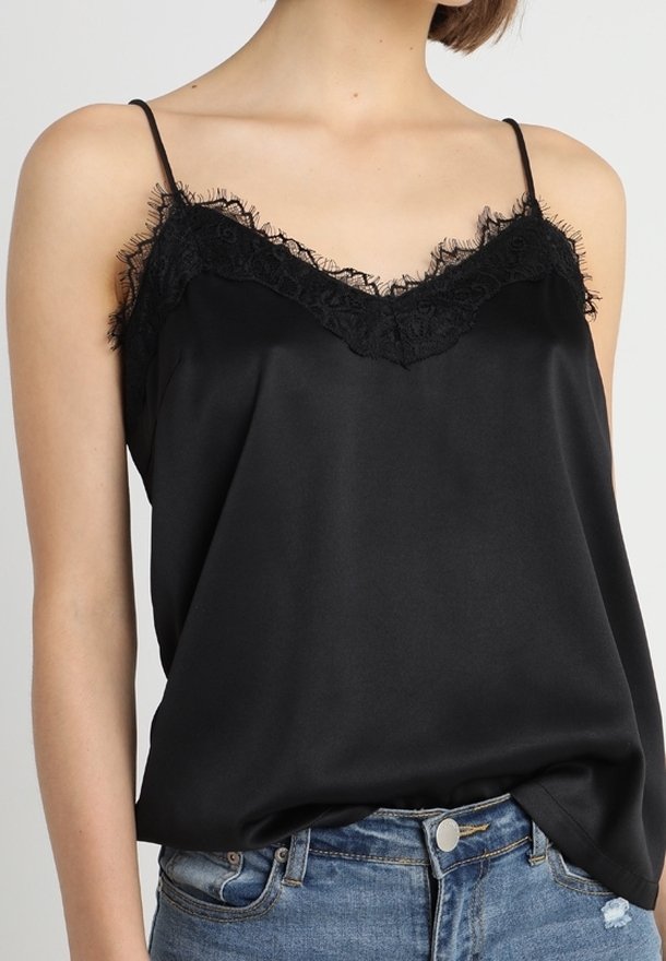 Camiseta de satén negro con encaje en el escote y tirantes ajustables, combinada con unos pantalones cortos de mezclilla descoloridos.