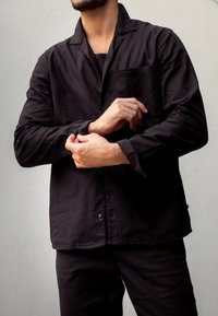 Czarna koszula z guzikami wykonana z teksturowanej tkaniny, z kieszonką na piersi i luźnym krojem. Długie rękawy są podwinięte, ujawniając prosty design.