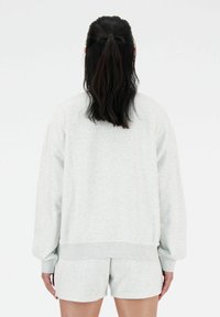 Sweatshirt gris clair à coupe décontractée et manches côtelées, assorti à un short. Texture douce, design simple, sans motifs ni matériels apparents.