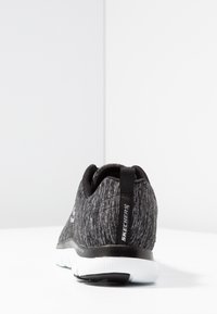 Buty Skechers z teksturowaną czarną i szaro-skalą cholewką, białą podeszwą, elastycznym designem oraz pętelką na pięcie ułatwiającą zakładanie.