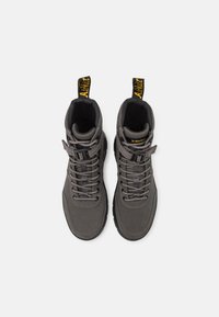 Botas altas grises de material suave con un acabado texturizado. Presentan cordones, costuras reforzadas y un destacado logo amarillo en las lengüetas del talón.