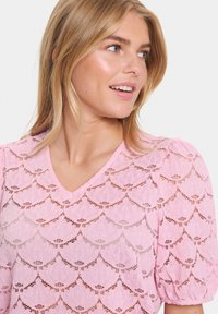 Top in pizzo rosa con scollatura a V, maniche a sbuffo e intricato motivo a onde. La texture leggera mette in evidenza l'abilità artigianale dettagliata.