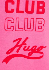 Tessuto rosa con testo rosso audace: "CLUB CLUB" in maiuscolo con un carattere arrotondato e "Hugo" in uno stile corsivo sottostante.