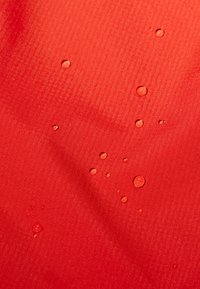 Tessuto rosso, idrorepellente, con una superficie strutturata, caratterizzato da numerose gocce d'acqua disperse sulla materia.