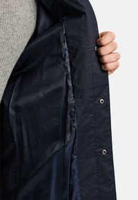 Jakna mornarsko plave boje s glatkom unutarnjom postavom. Ima metalni zatvarač na pritisak i teksturiranu vanjsku površinu. Jednostavan i funkcionalan dizajn.